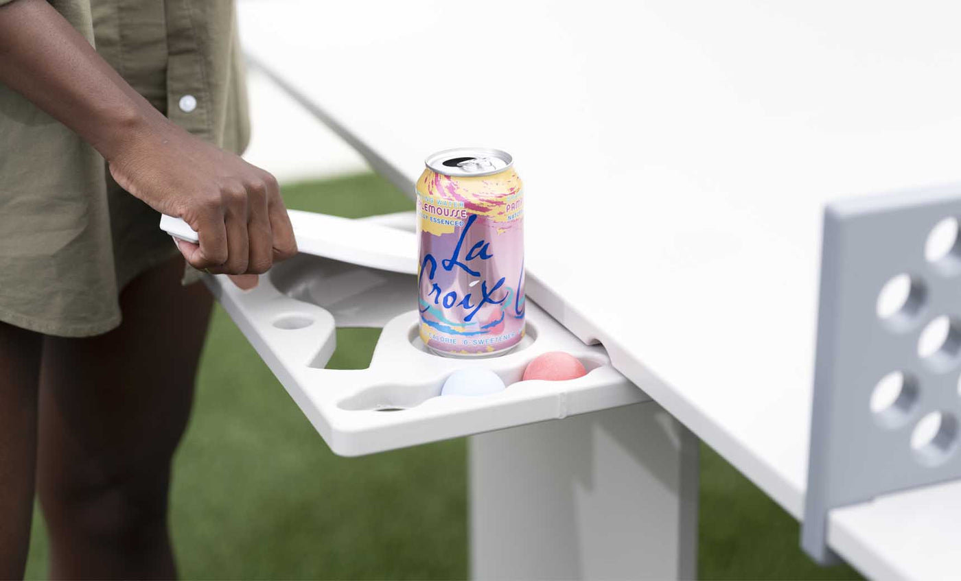 White pull-out side tray with molded drink and accessory holders beneath an outdoor ping pong table.