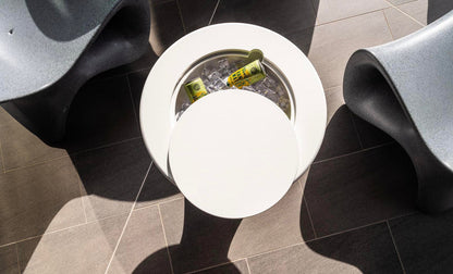 Round side table with built-in ice bucket holding canned drinks, surrounded by modern lounge chairs.