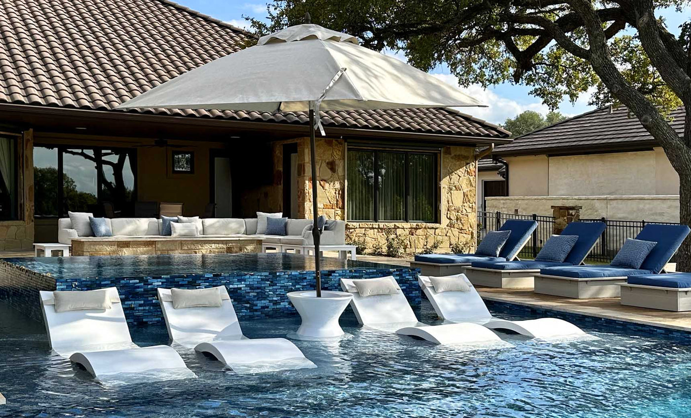 White poolside ice bin table holding an umbrella, partially submerged in shallow water beside a lounge chair.