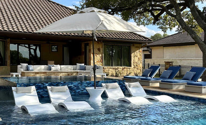 White poolside ice bin table holding an umbrella, partially submerged in shallow water beside a lounge chair.
