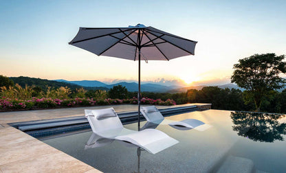 White chaise loungers beneath an umbrella in a luxury infinity pool overlooking mountains at sunset.
