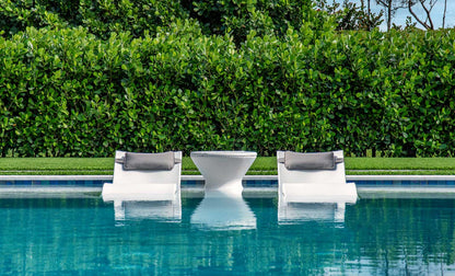 Two white in-pool lounge chairs with gray headrests and a white side table in shallow pool water.