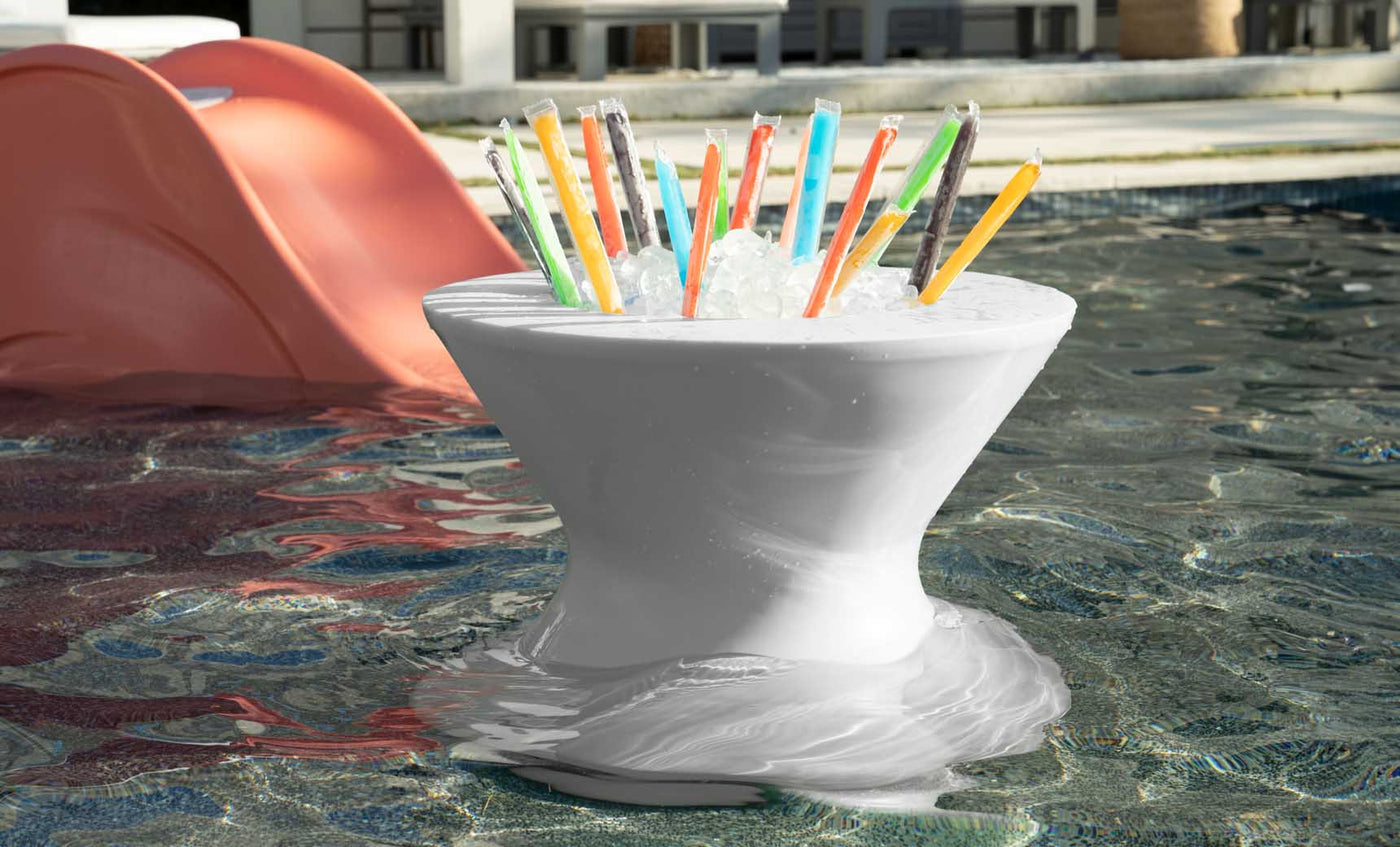 White poolside ice bin table filled with ice pops, partially submerged in shallow water beside a lounge chair.
