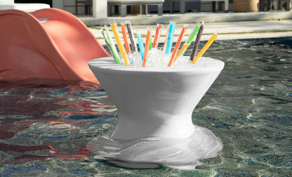 White poolside ice bin table filled with ice pops, partially submerged in shallow water beside a lounge chair.