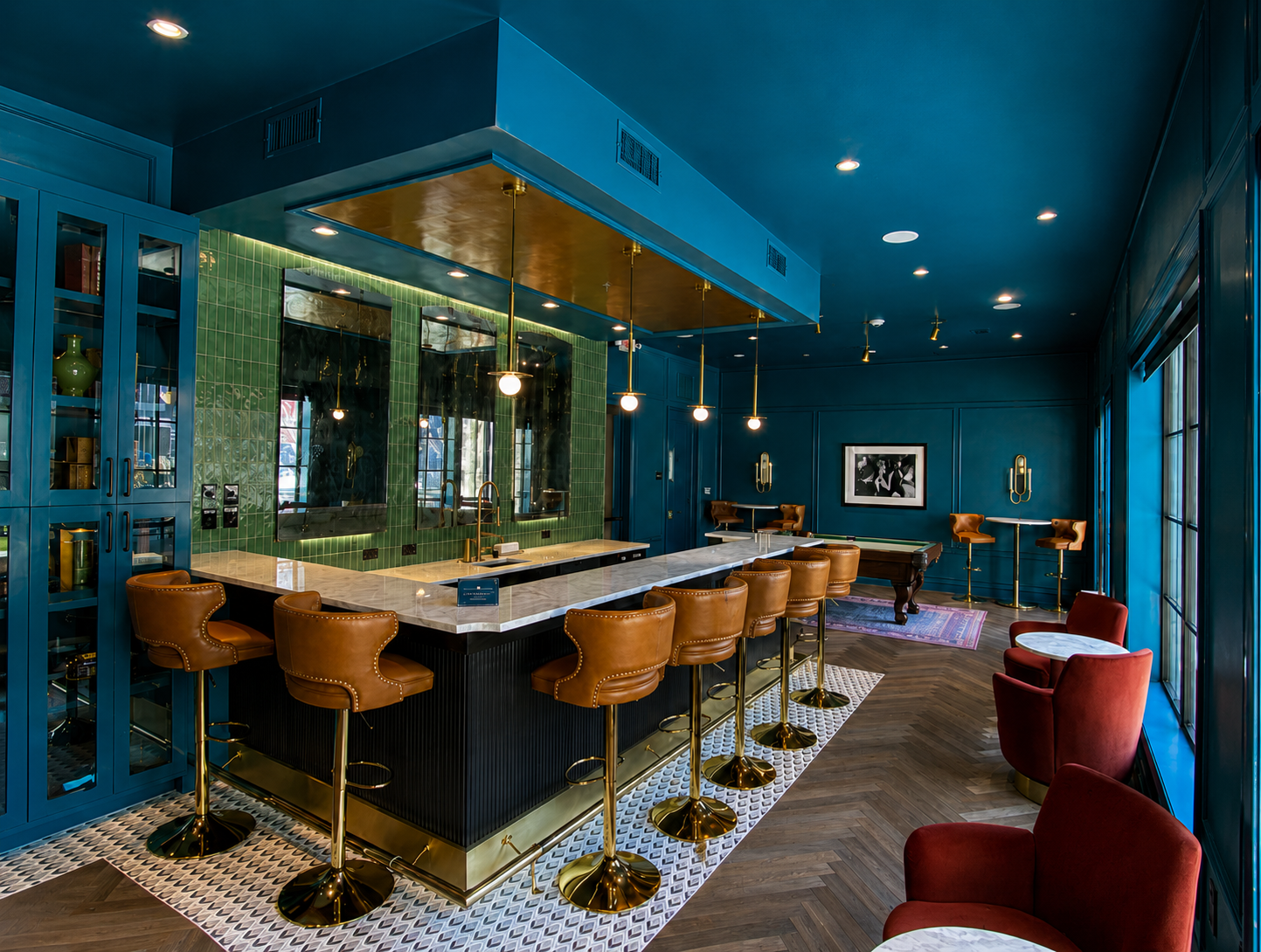 Modern bar interior with blue walls, wooden bar stools, and red chairs.