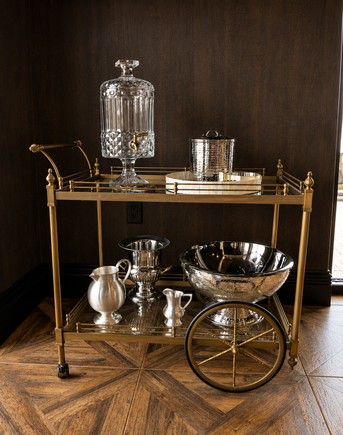 Gold bar cart with silver and glass barware against a dark wall.