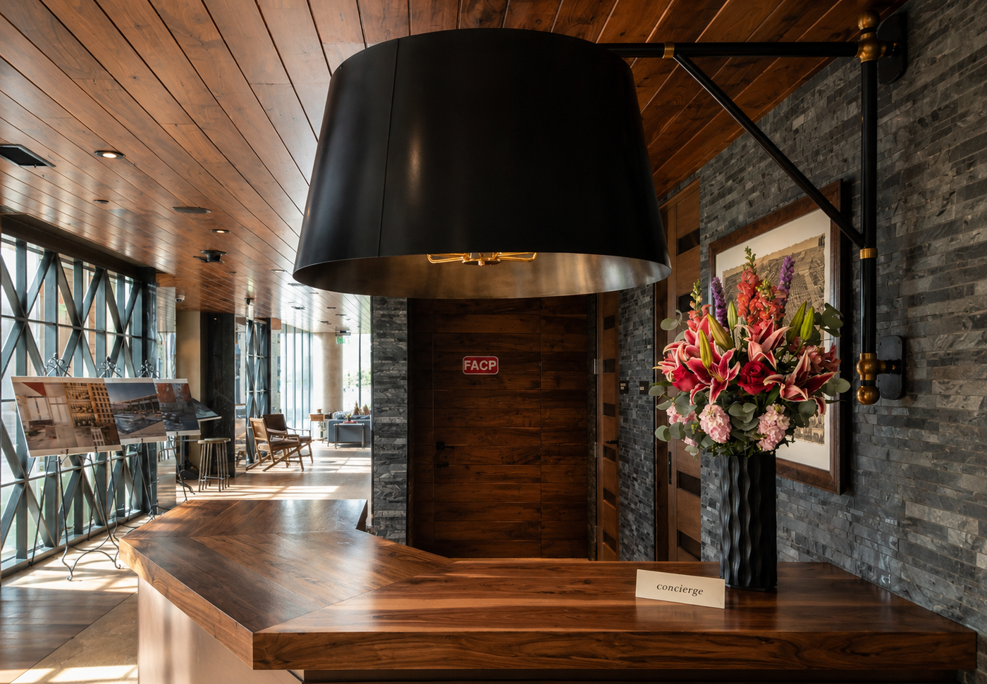 Modern concierge area with wooden counter, large black pendant light, and decorative flowers.