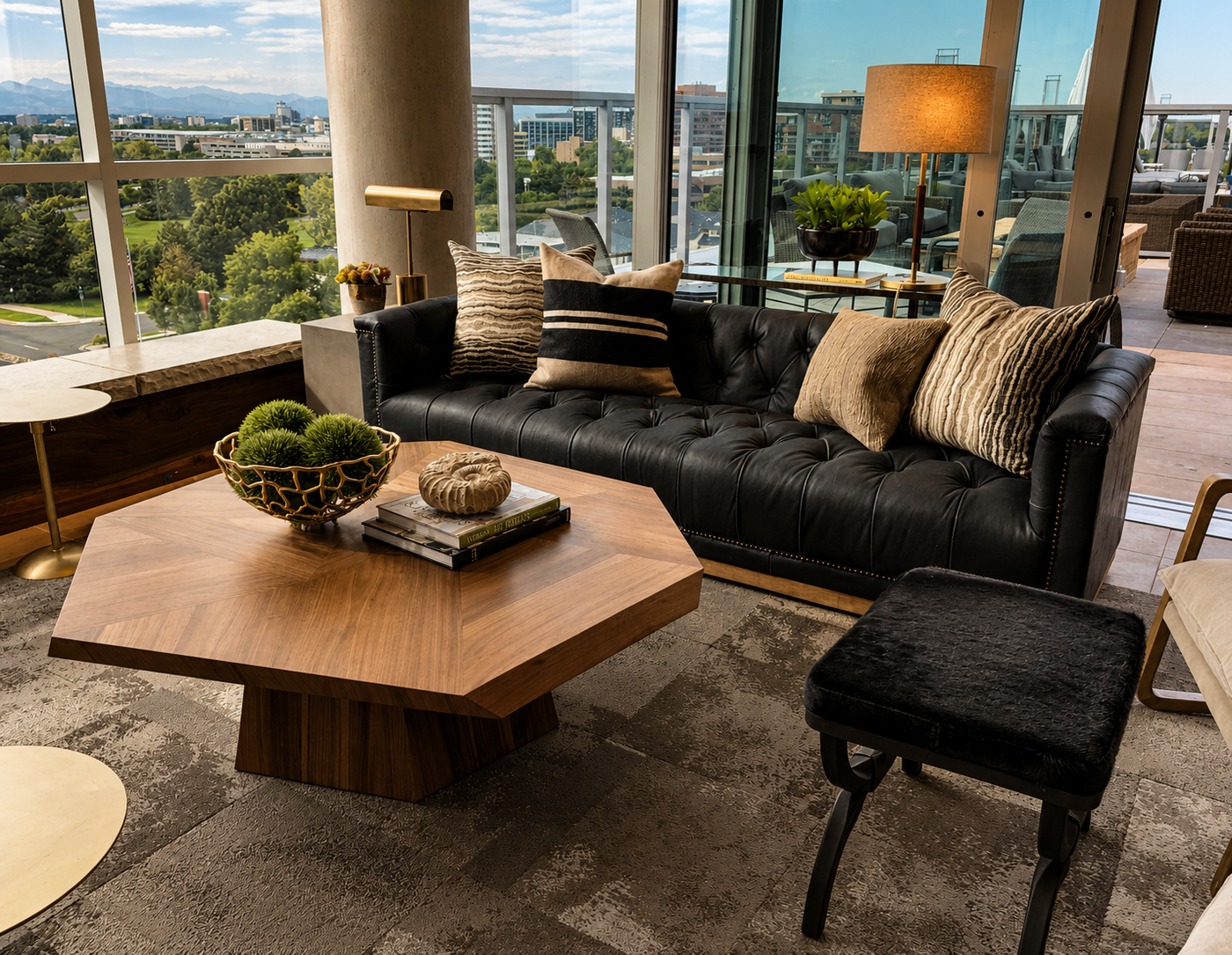 Modern lounge at club with a black tufted sofa, wooden coffee table, and large windows.