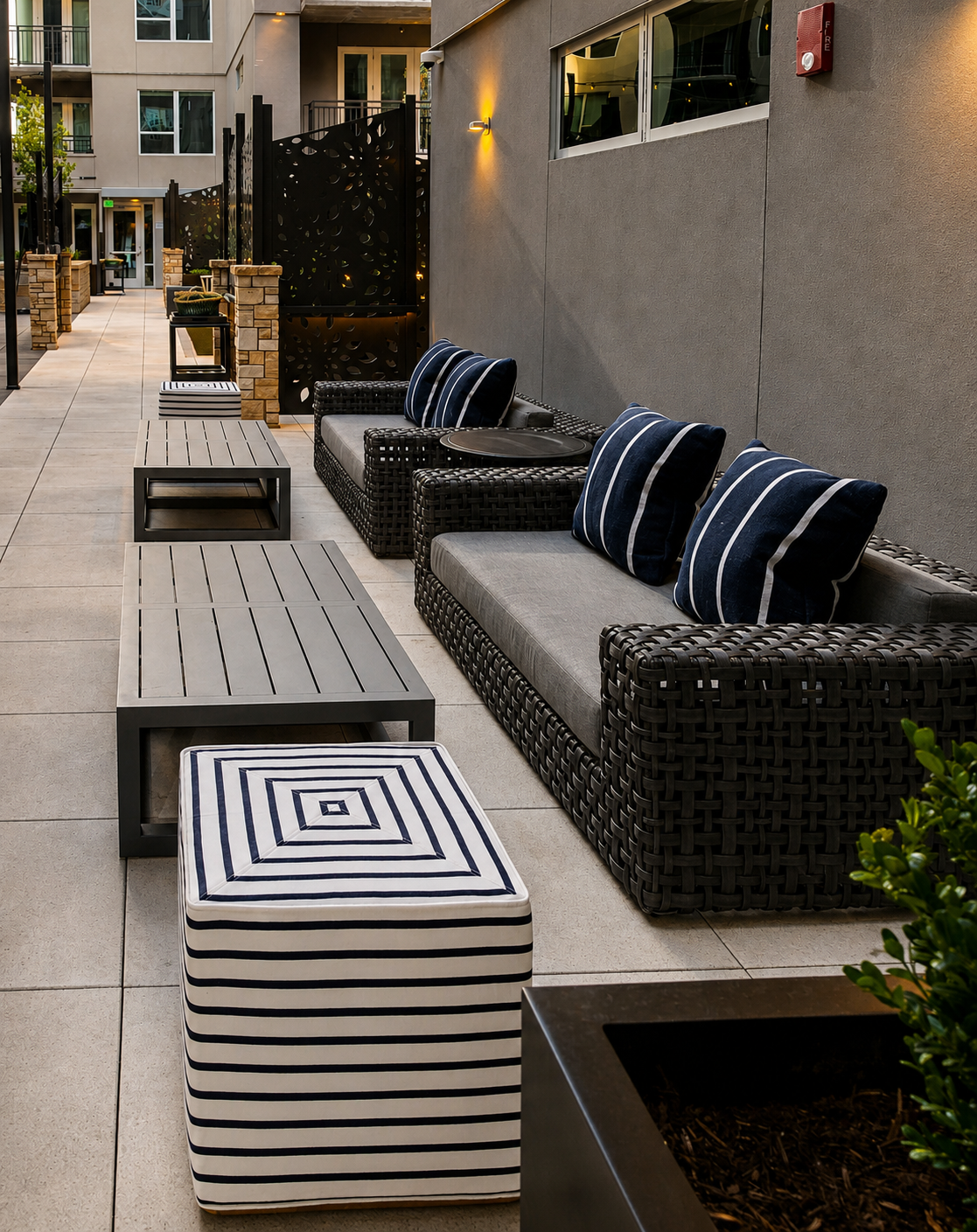 Outdoor patio with wicker furniture, striped ottoman, and building in the background