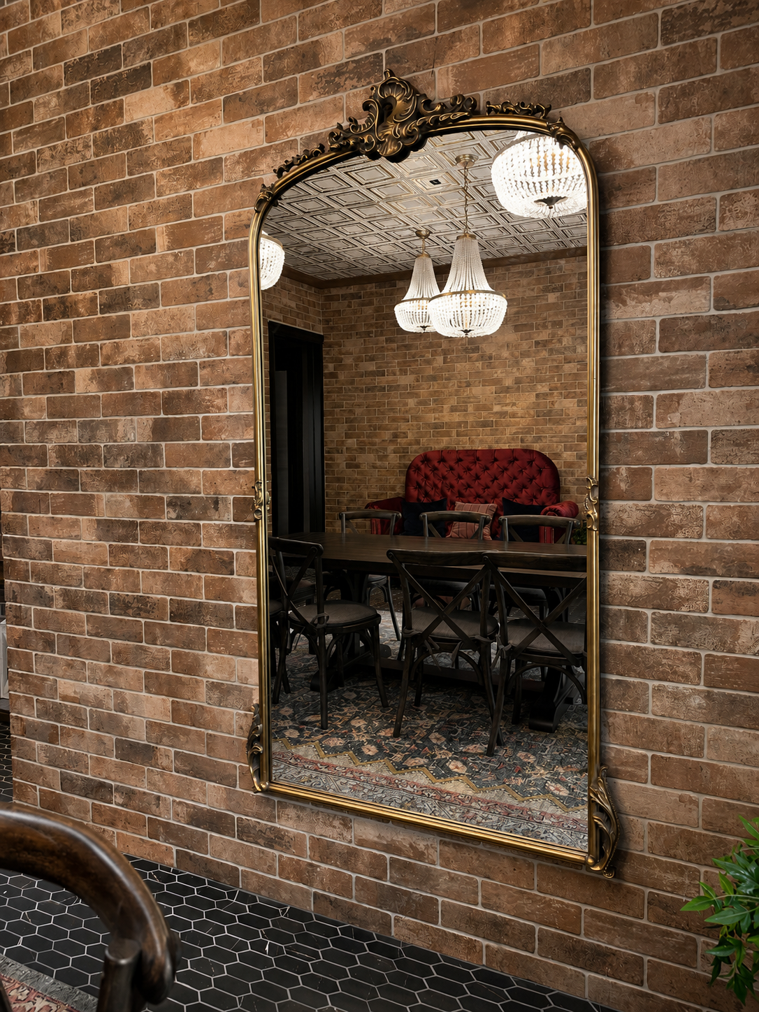 Decorative mirror on a brick wall reflecting an interior setting with a red sofa and chandelier.