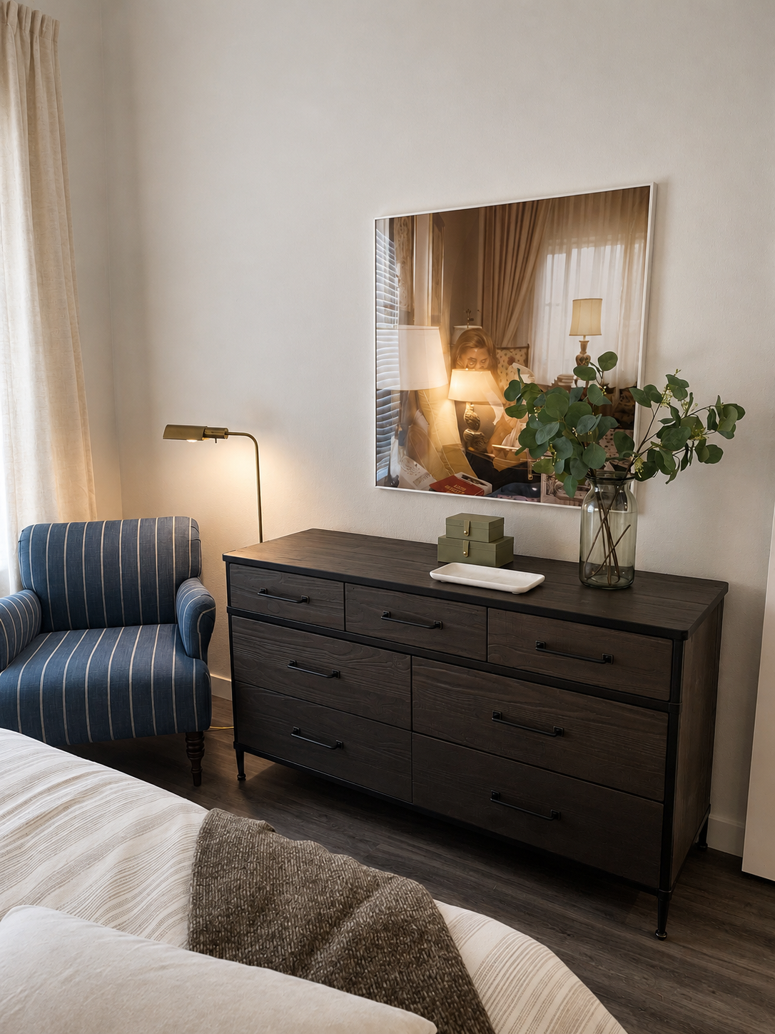 Modern bedroom with dark wood dresser, striped armchair, and large mirror.