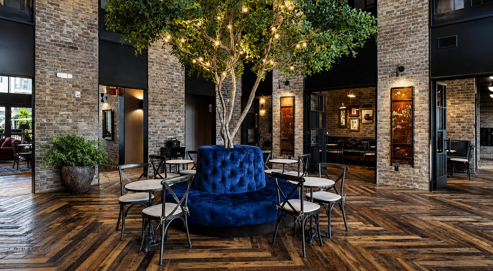 Indoor setting with a blue cushioned chair, and a large faux tree in the middle, wooden floor, and brick walls.