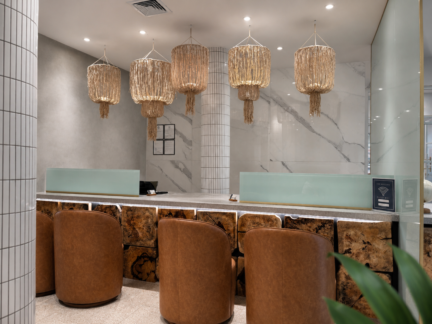 Modern leasing desk with chandelier lights, brown stools, and a marble wall.
