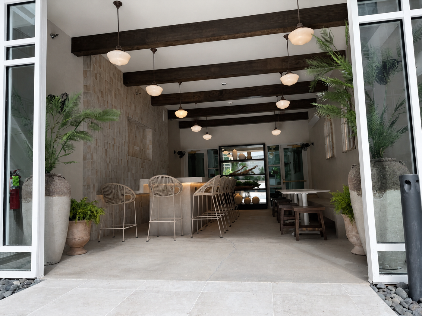 Modern indoor-outdoor space with wooden beams, potted plants, and a dining area.