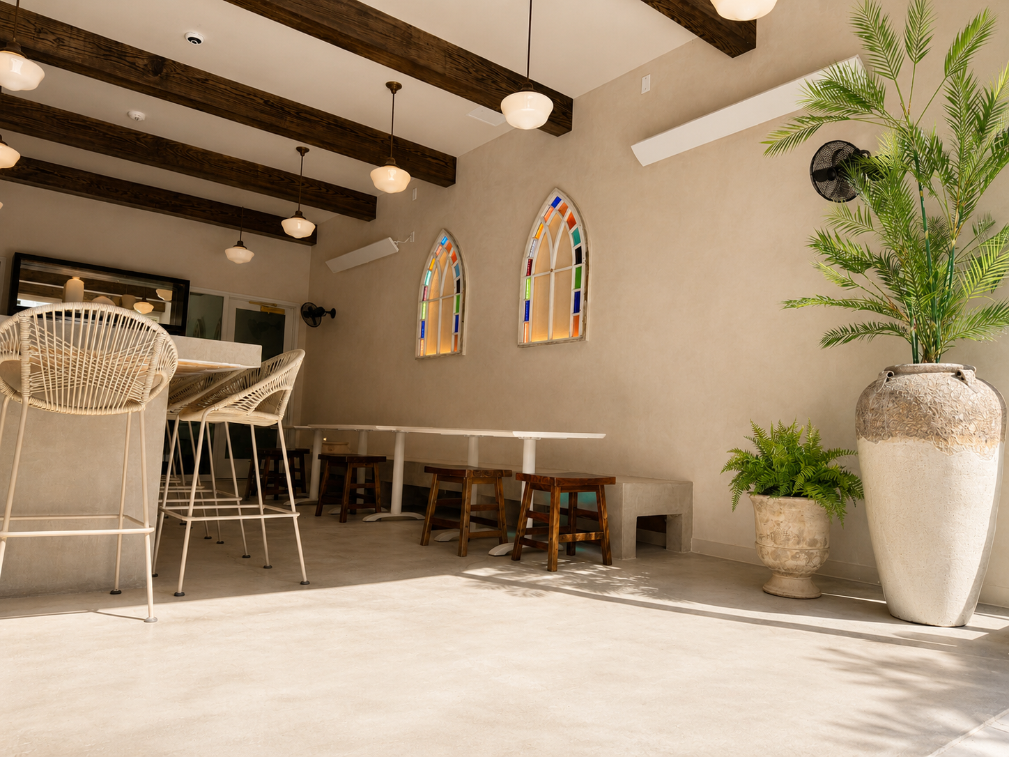 Modern interior with white tables and chairs, stained glass windows, and decorative plants.