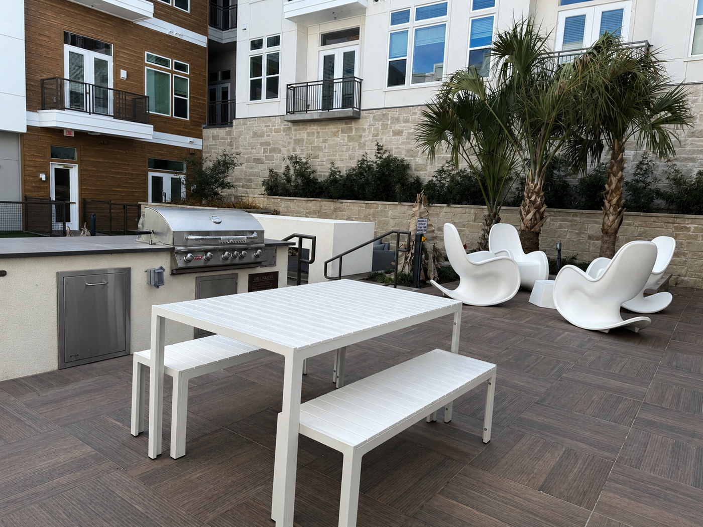 Outdoor patio area with white table, chairs, and benches in front of a building.