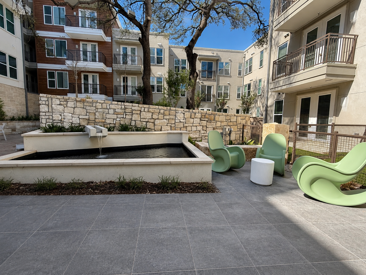 Outdoor courtyard with a fountain and green chairs in front of apartment buildings.