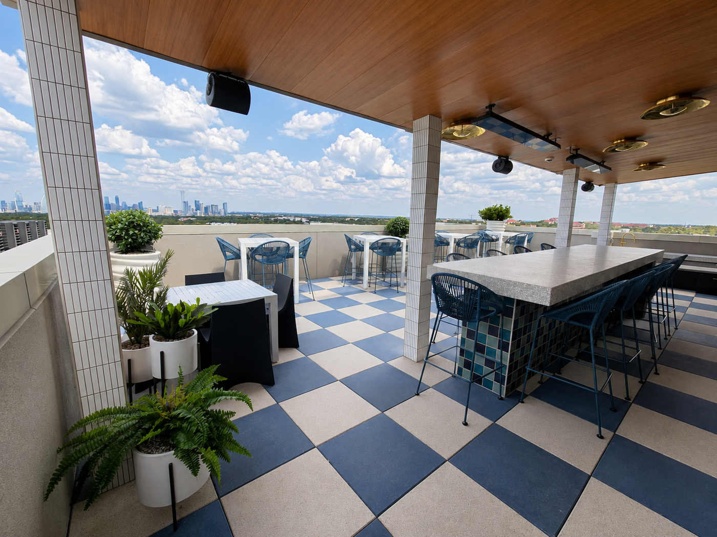 Outdoor rooftop area with checkered floor, tables, and chairs with a cityscape view.