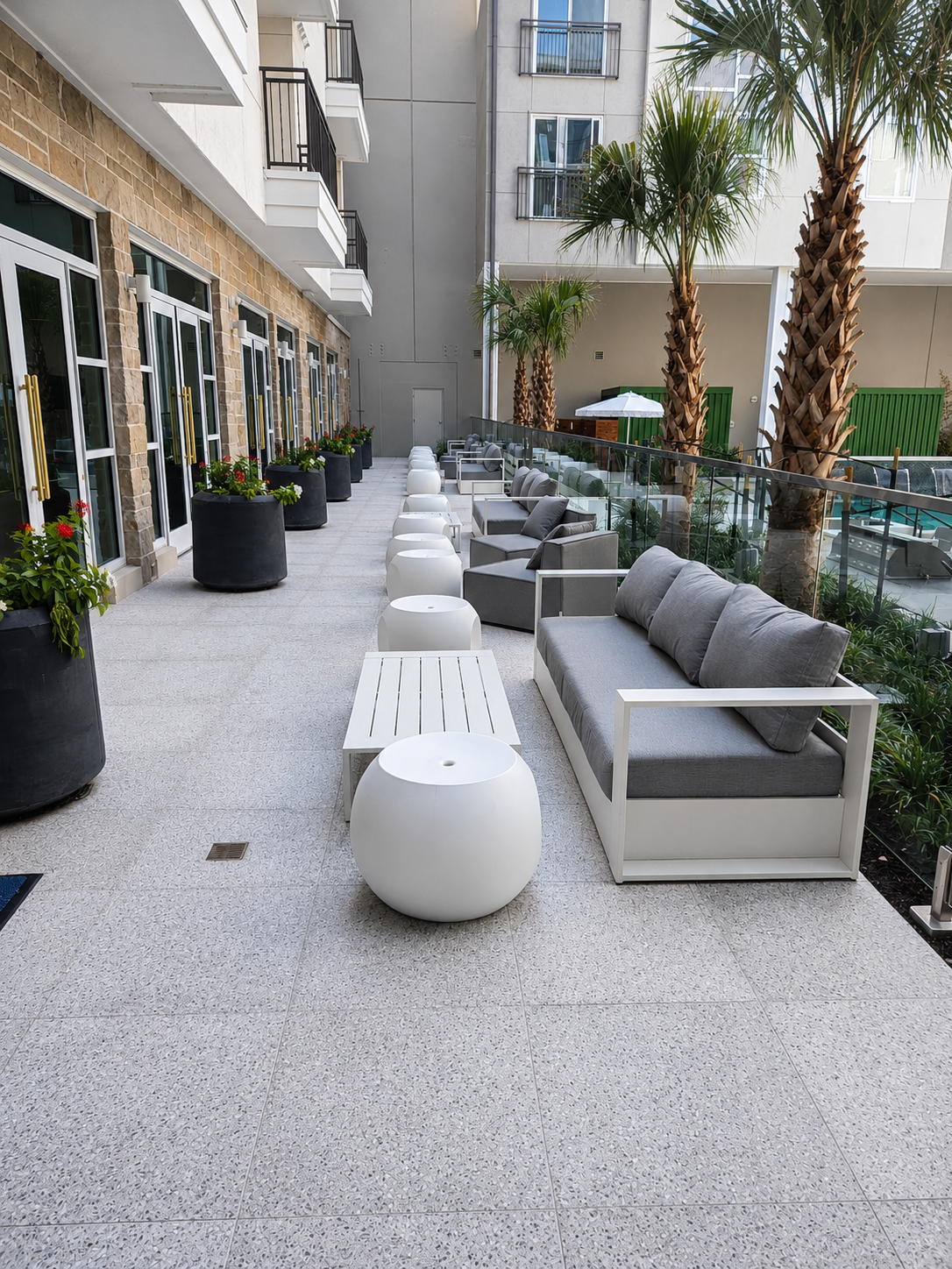 Outdoor seating area with gray cushioned sofas and white spherical tables in a modern building courtyard.