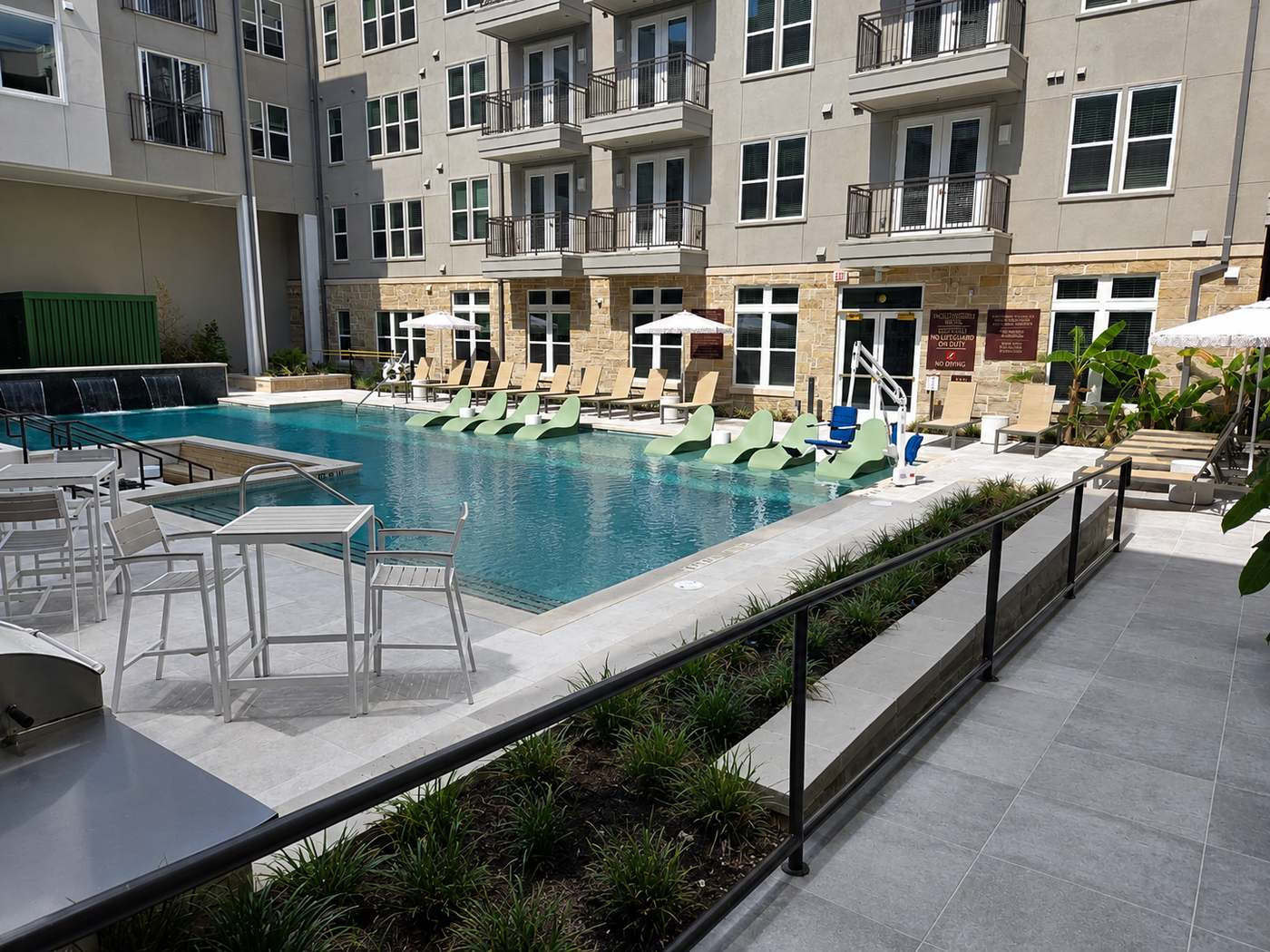 Outdoor pool area with lounge chairs, tables, and umbrellas in a residential complex.
