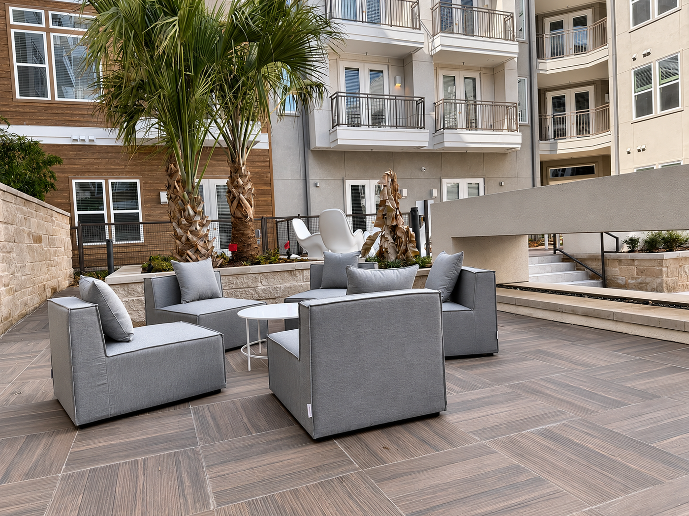 Outdoor patio area with gray furniture and palm trees in front of a building.