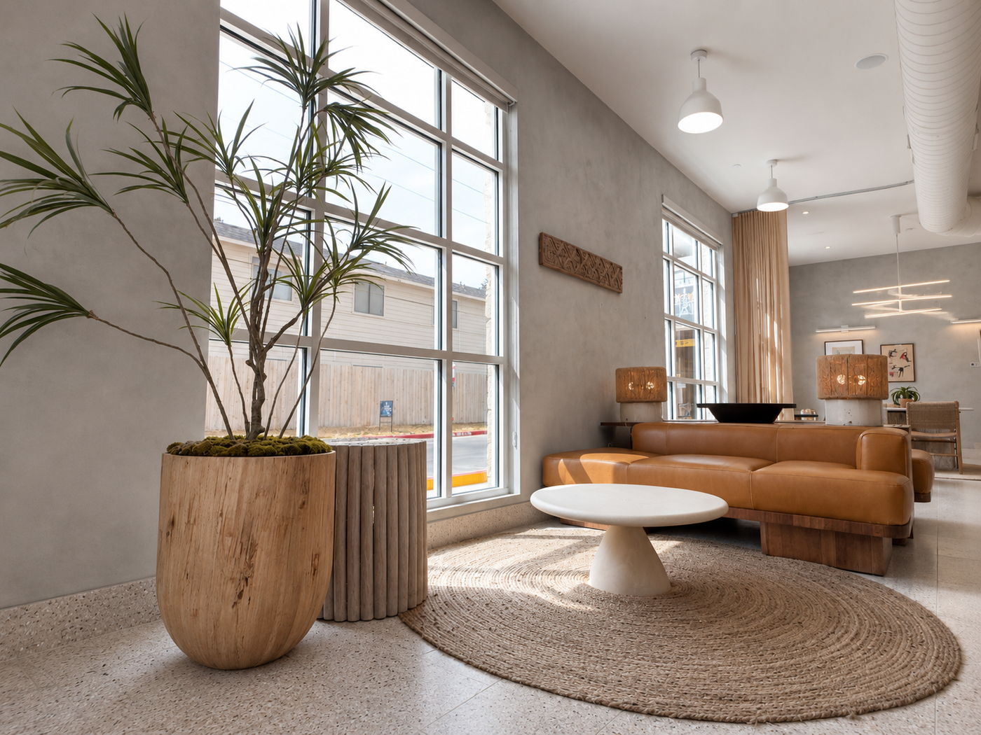 Modern leasing waiting area with a large window, brown sofa, white coffee table, and potted plant.