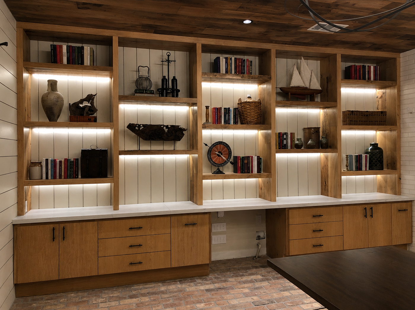Wooden bookshelf with built-in lighting and desk area in a room with wooden ceiling.