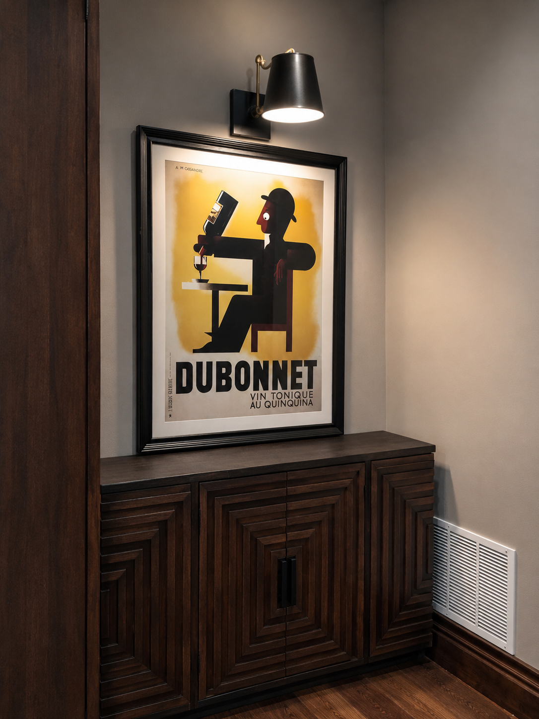 Framed poster of a man with a drink on a wall above a wooden cabinet.