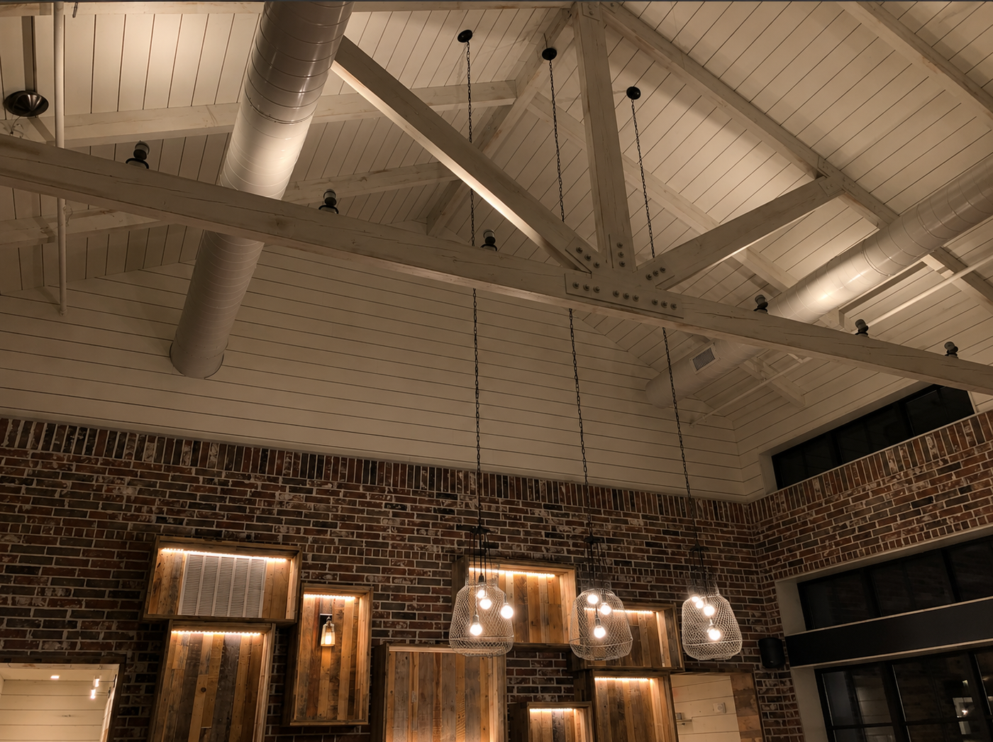 Indoors setting with wooden beams, brick wall, and hanging lights.